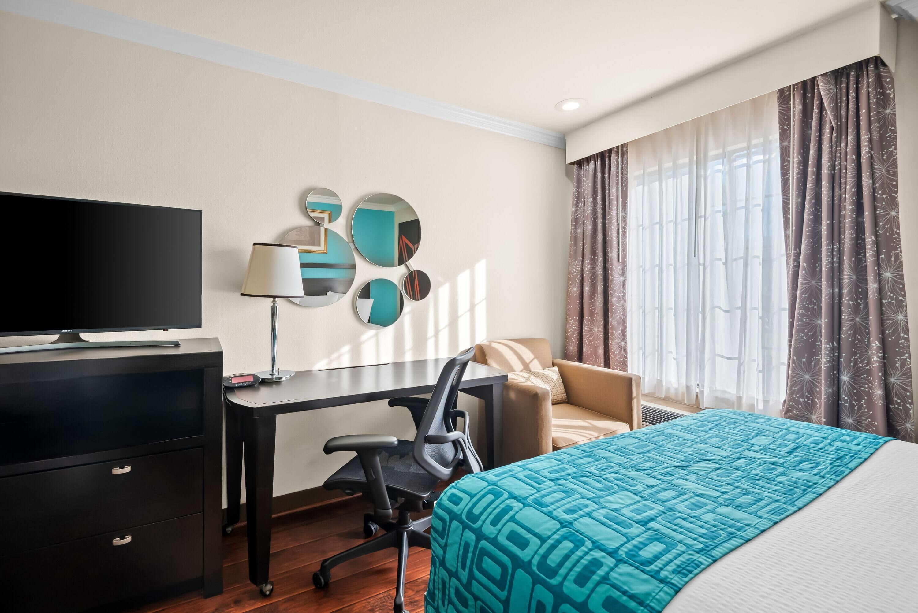 Hotelkamer met een bed, een bureau met stoel, een televisie en een muur met decoratieve spiegels.