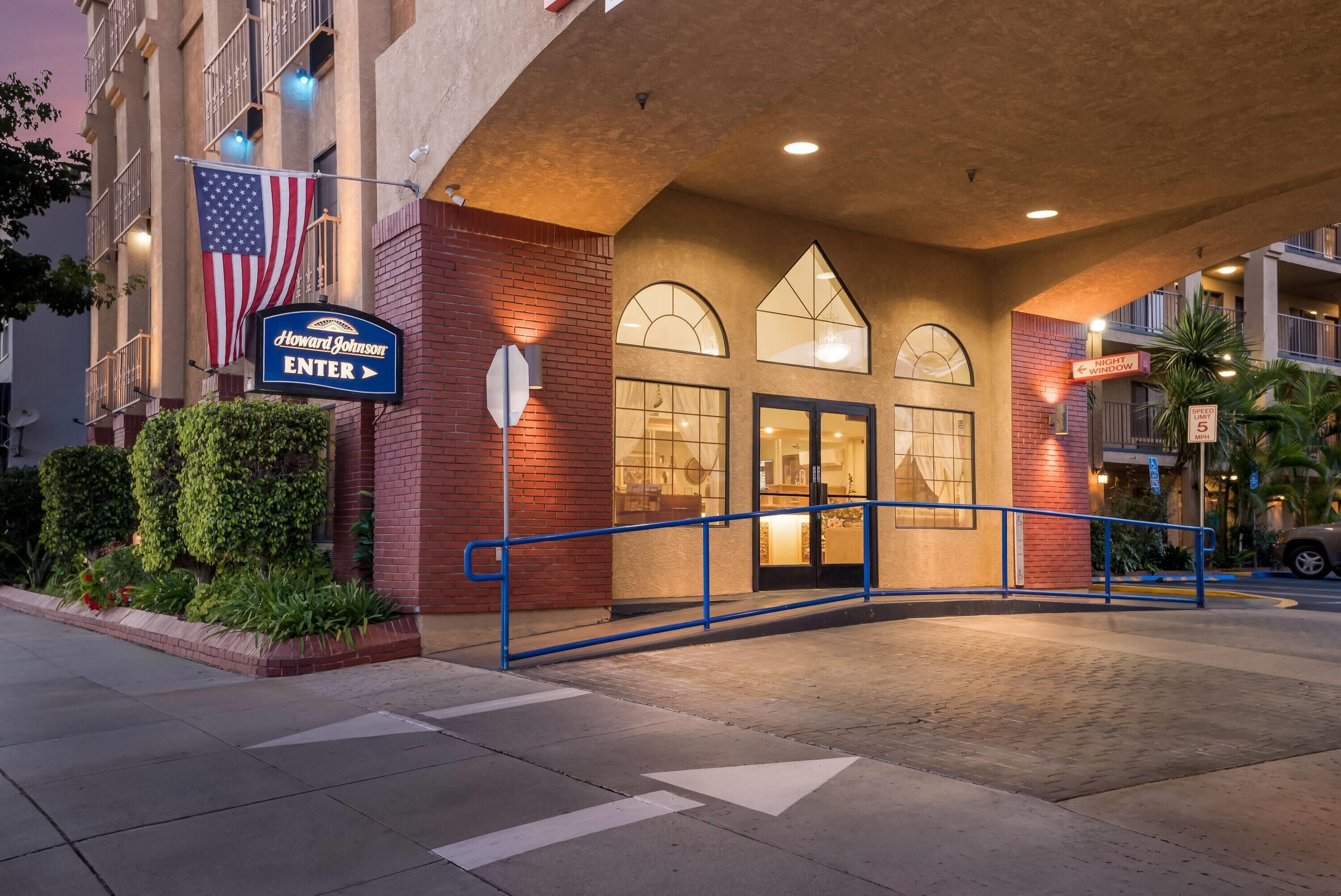 A hotel entrance with a sign reading "Howard Johnson ENTER", an American flag, and a speed limit sign of 5 mph.