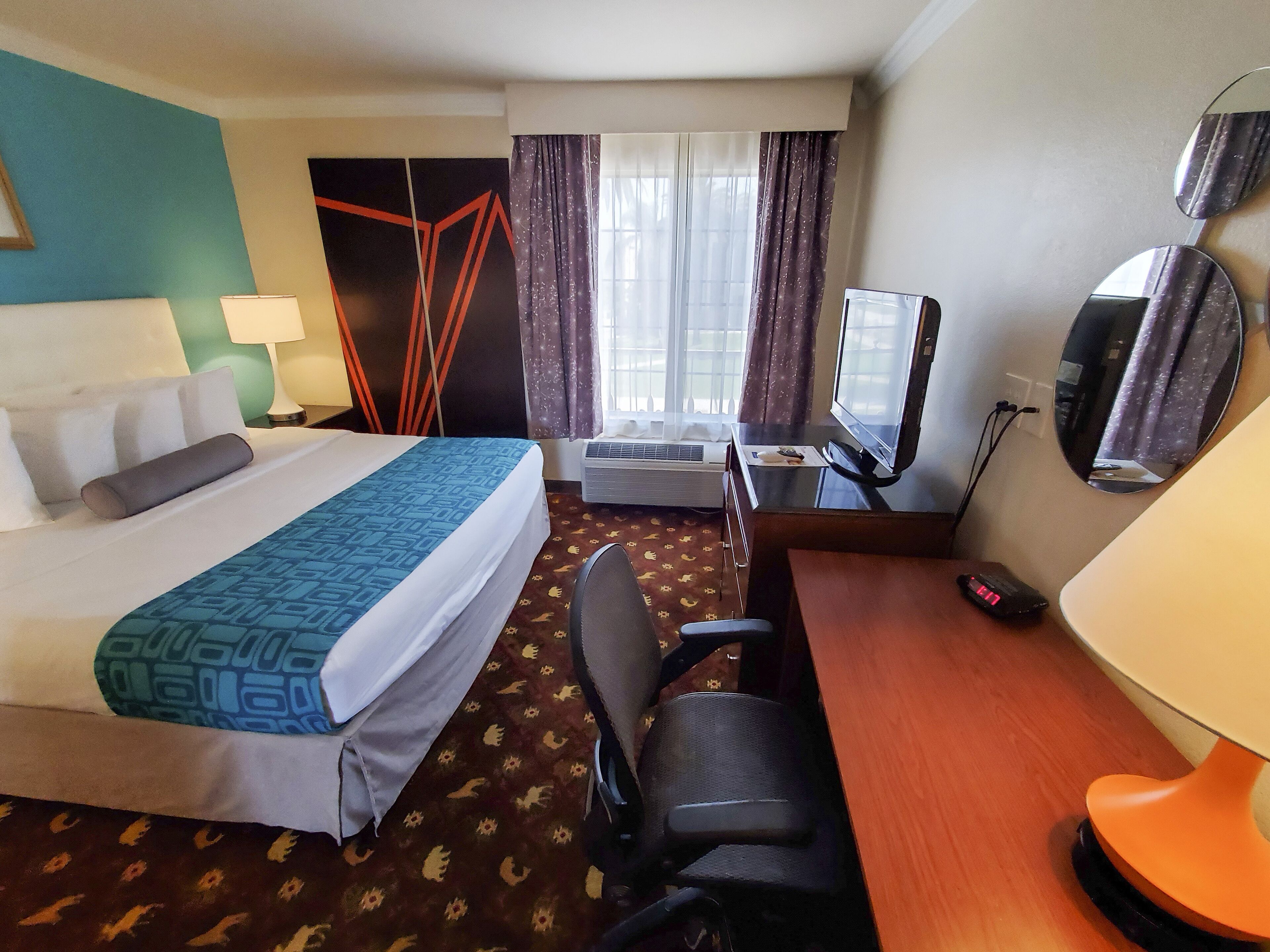 A hotel room with a bed, desk, chair, TV, and a mirror.