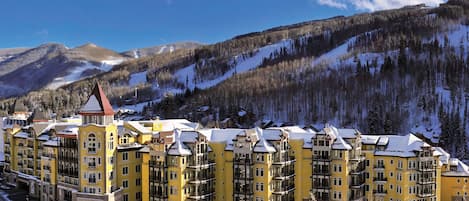 A multi-story hotel with a yellow facade, located in a mountainous area with snow-covered slopes.
