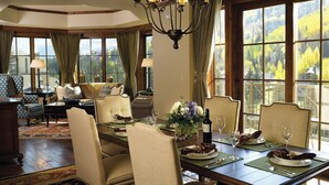 A dining room with a large table set for six, surrounded by six chairs. There is a chandelier above the table, and the room has large windows with a view of trees. - The Ritz-Carlton Club, Vail (Vail)