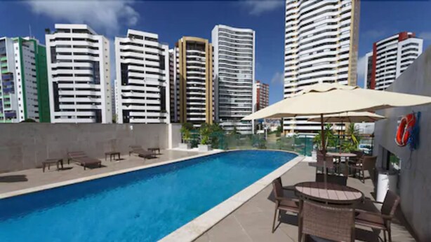A rooftop pool with lounge chairs and umbrellas, surrounded by high-rise buildings.