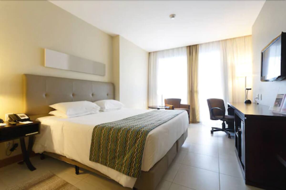 A hotel room with a large bed, a desk, a chair, and a television.
