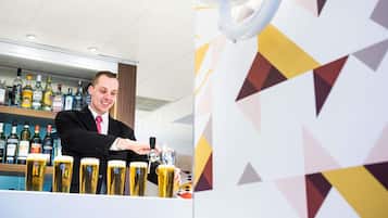 A bar area with a bartender pouring beer into glasses, shelves with various liquor bottles, and a geometric patterned wall.