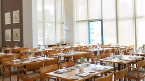 A spacious dining area with multiple tables and chairs, large windows allowing natural light, and framed artwork on the walls.