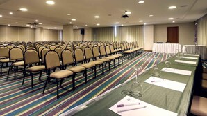 A conference room with rows of chairs, a projector screen, and a table with a green tablecloth and wine glasses.