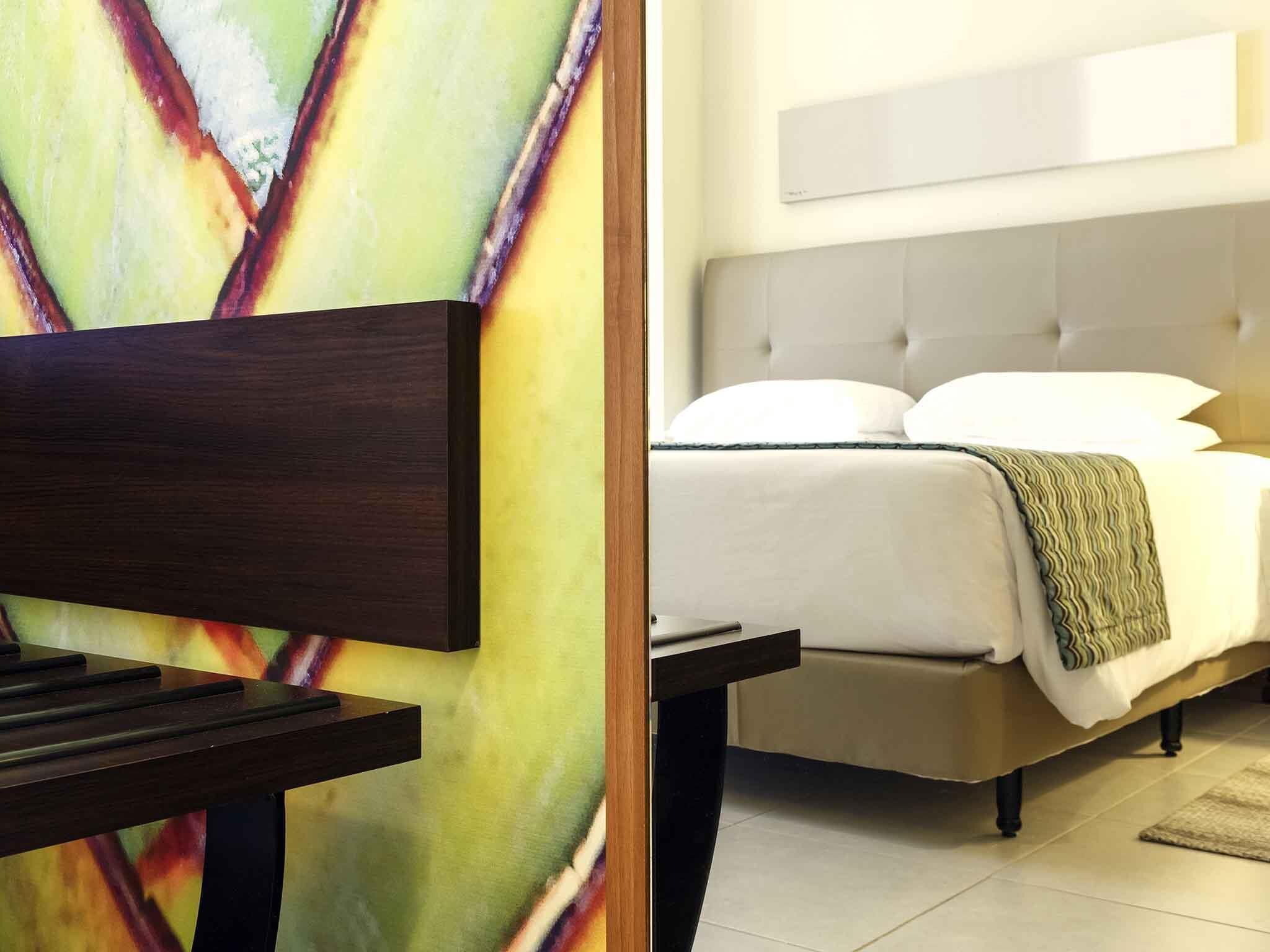 A hotel room with a bed, a television on a stand, and a large abstract painting on the wall.