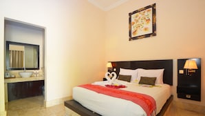 A hotel room with a large bed, a bathroom with a sink and mirror, and a framed picture on the wall. - Andari Legian (Legian)