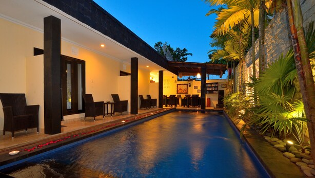 A pool area with chairs and a dining area, surrounded by plants and a stone wall. - Andari Legian (Legian)