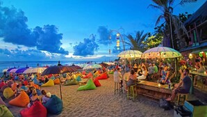 A beach with colorful bean bags and umbrellas, a bar area, and palm trees. - Andari Legian (Legian)