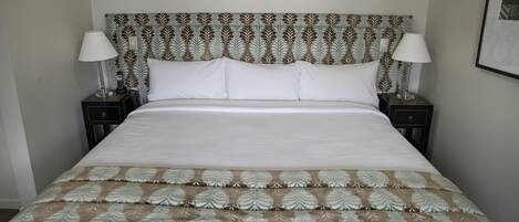 A neatly made bed with a patterned bedspread, two bedside tables with lamps, and a patterned headboard.