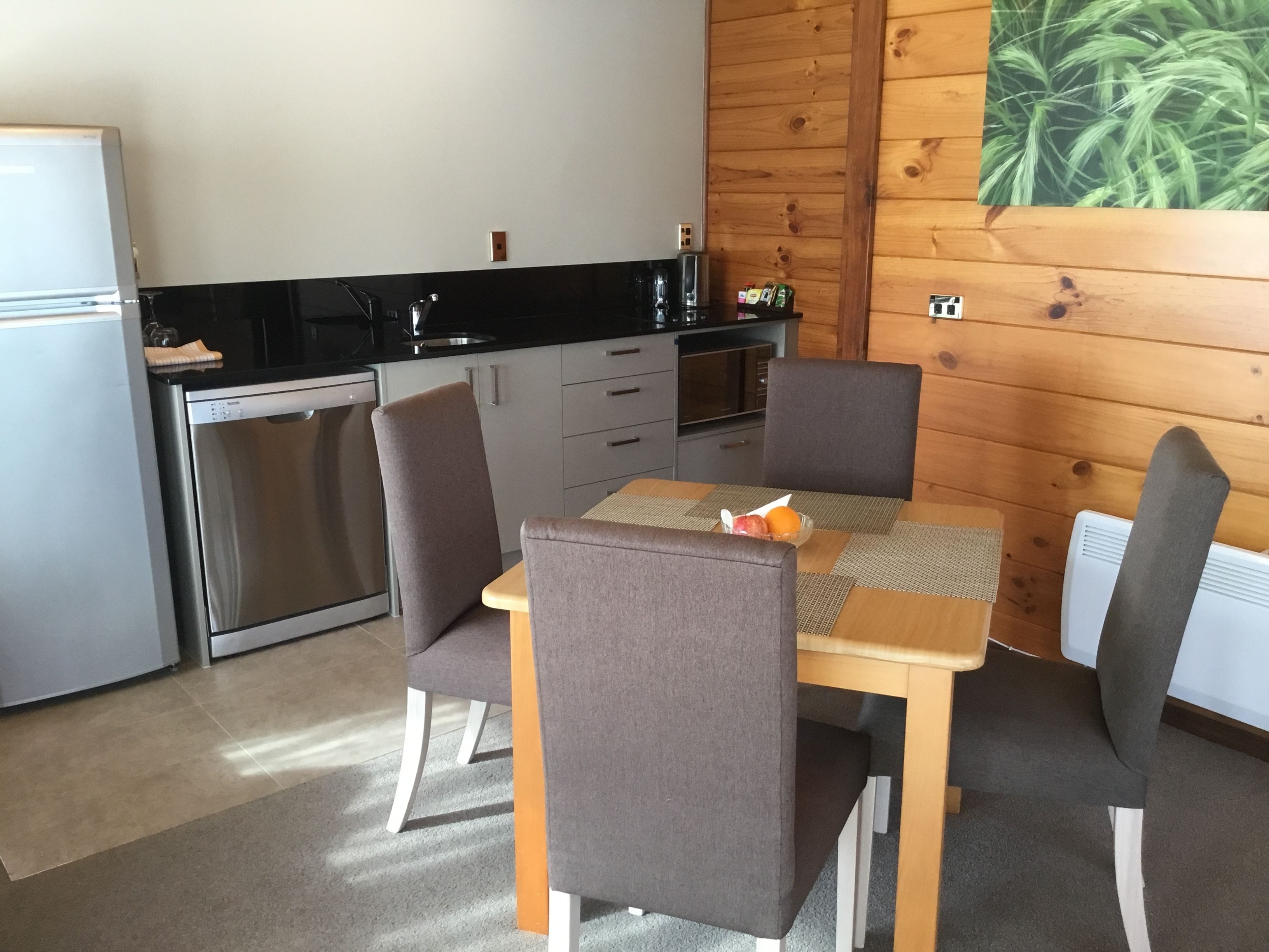 Una cocina compacta con refrigerador, microondas y estufa. Hay una mesa de comedor con cuatro sillas y un frutero pequeño encima.