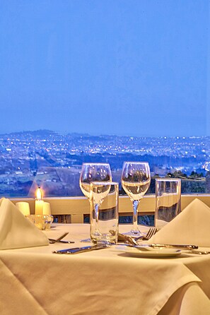 A table set for dining with a candle, three wine glasses, and cutlery, overlooking a cityscape at dusk. - Waitakere Resort & Spa (Auckland)