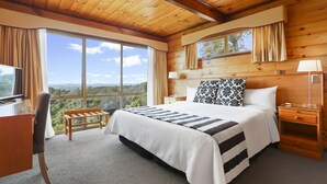 A bedroom with a large bed, a desk, and a view of the outdoors. - Waitakere Resort & Spa (Auckland)