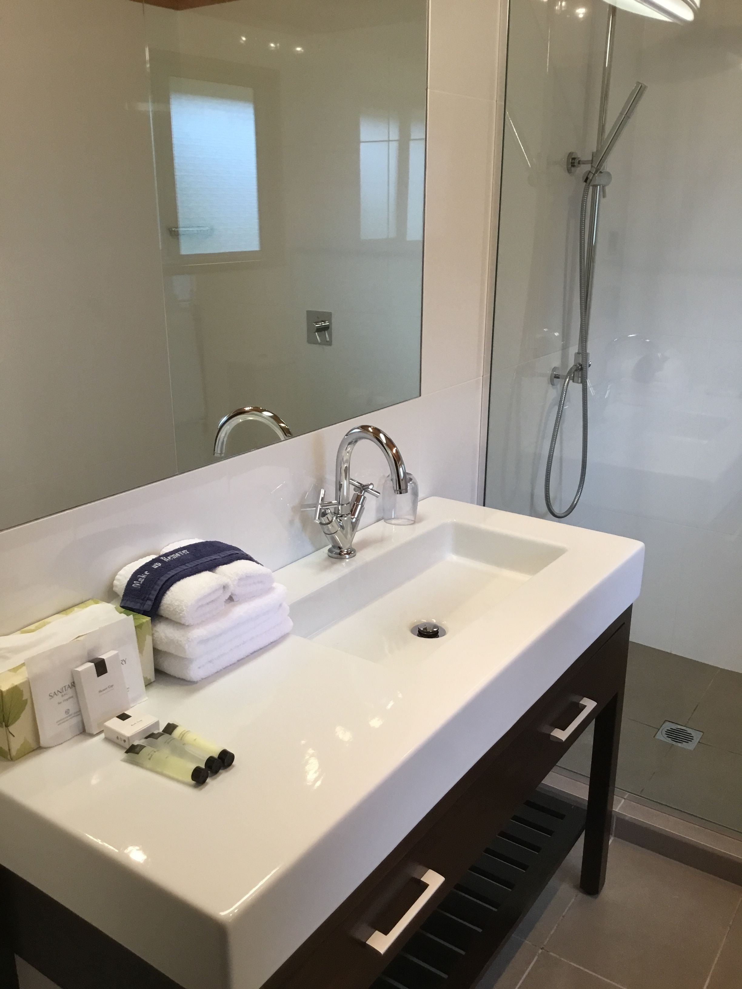 Un baño moderno con un lavamanos grande de color blanco, un espejo y una ducha con mampara de vidrio.