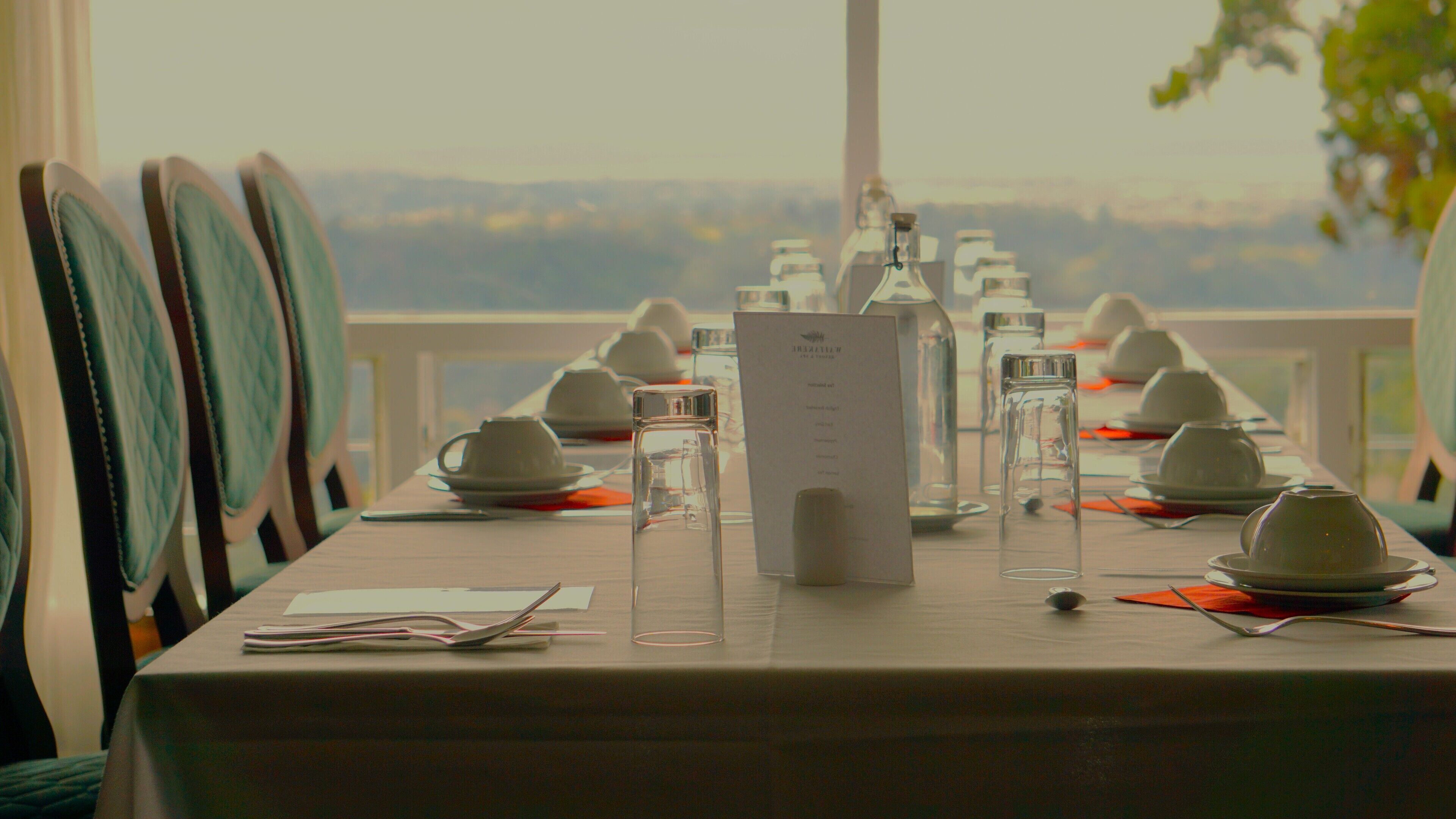 Une table dressée pour un repas, avec un menu, des verres et des théières, offrant une vue panoramique.