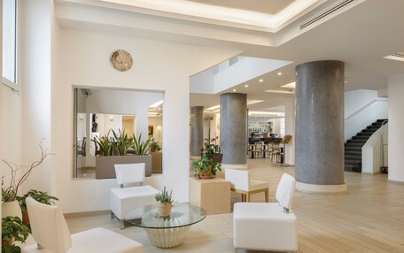 A spacious lobby with white furniture, large columns, and potted plants.