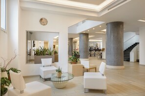 Un vestíbulo amplio con mobiliario blanco, columnas grandes y plantas en macetas.