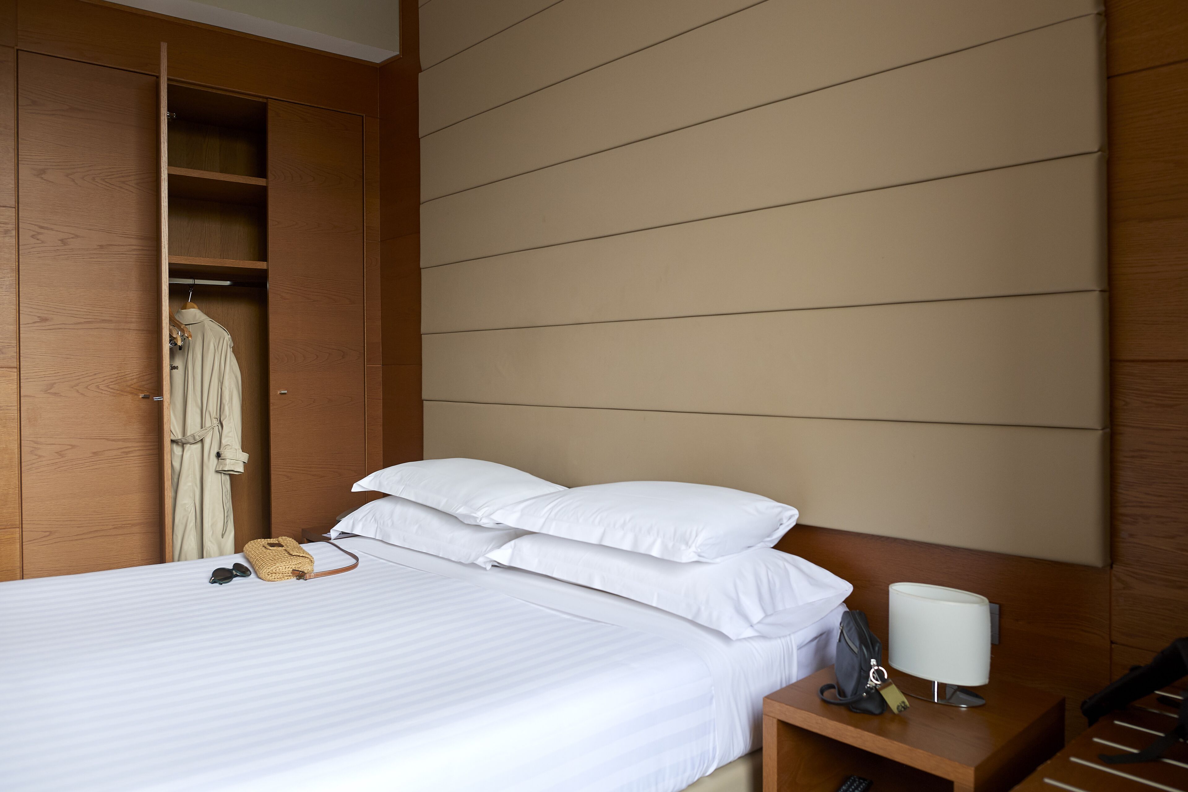 A hotel room with a bed, a bedside table with a lamp, a telephone, and a coat hanging on a rack.