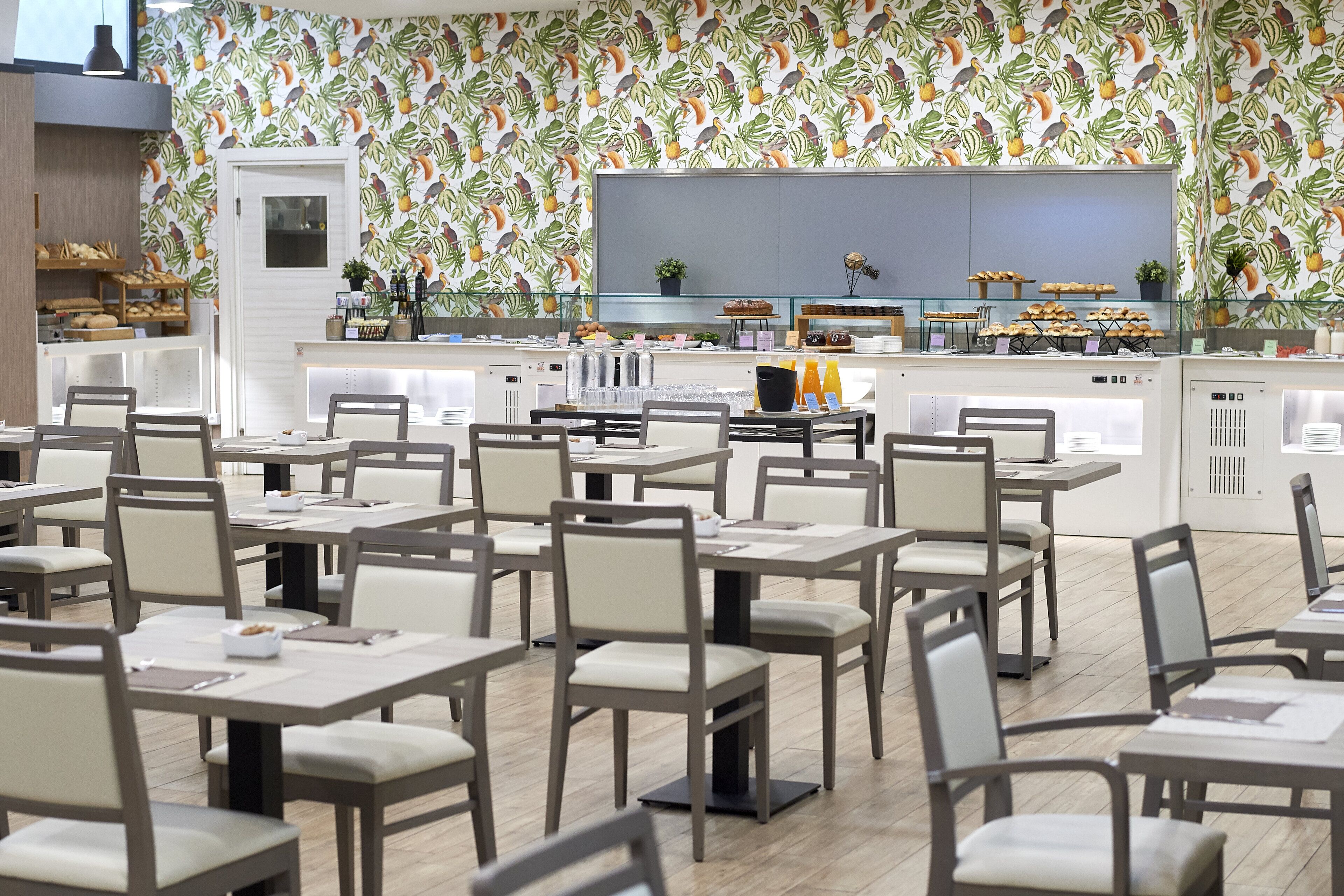 En restaurant med flere borde, stole, et køkkenområde og en væg med et mønster.
