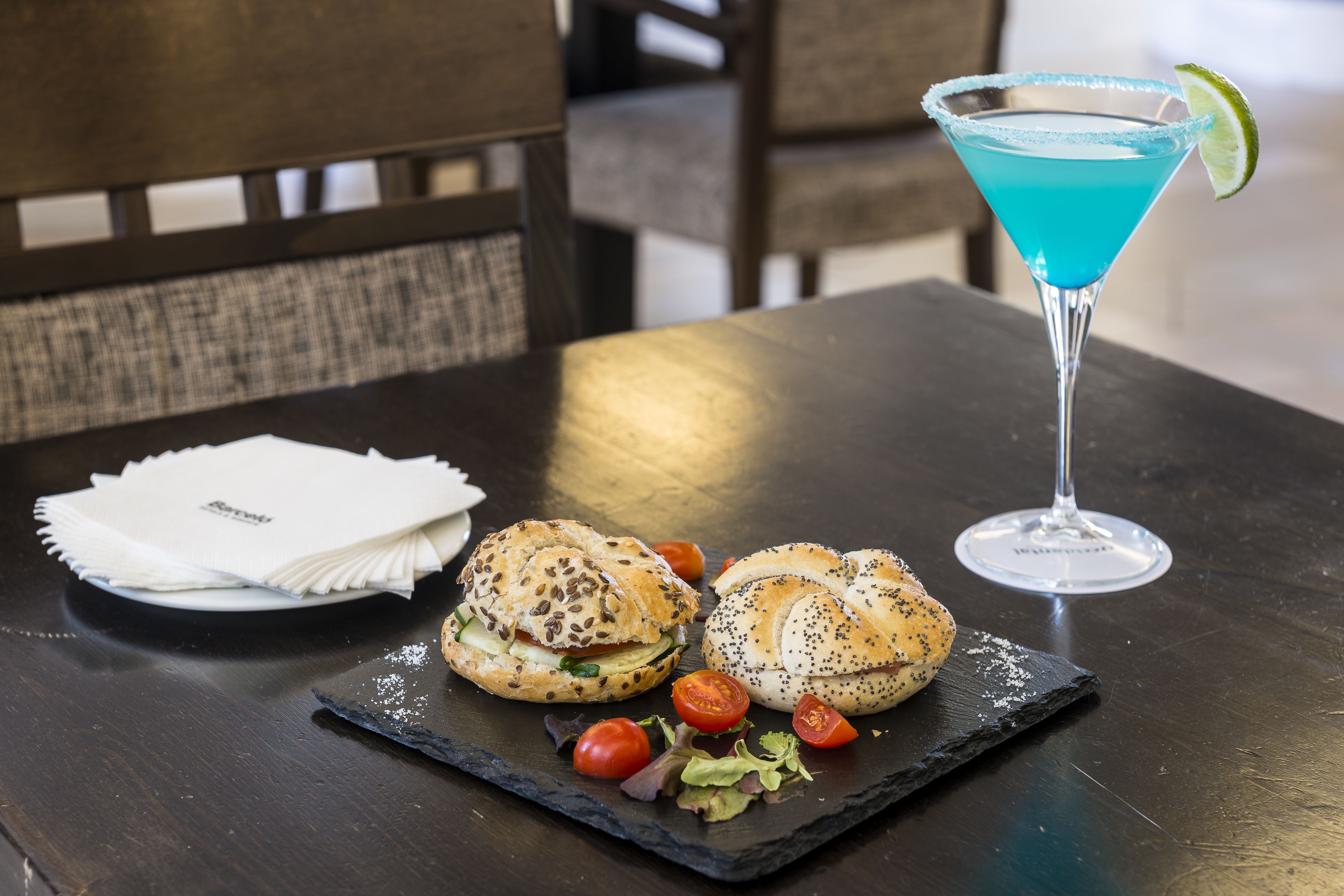 Una mesa con dos bagels, una copa de martini y un plato de servilletas dobladas.