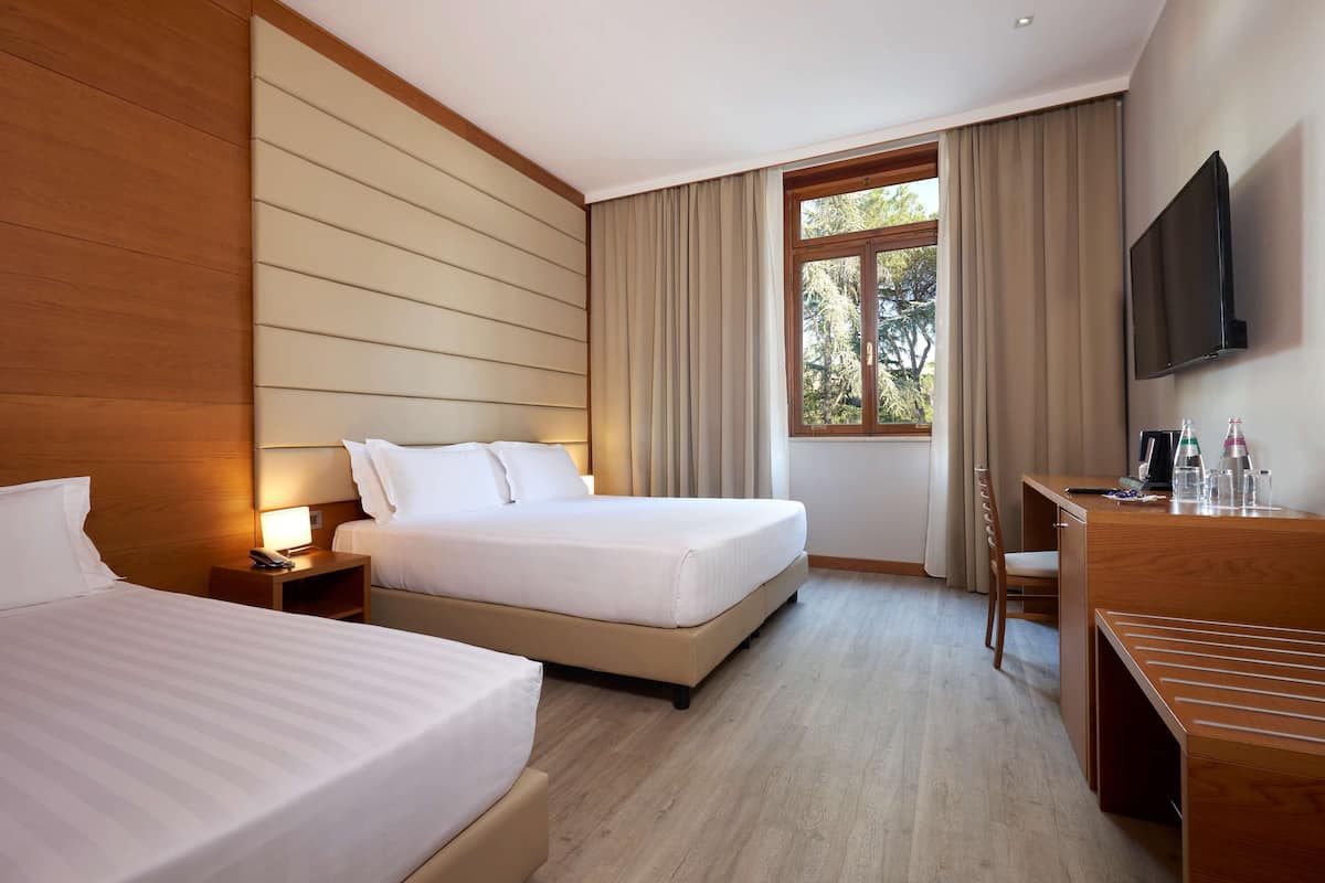 Habitación de hotel con dos camas, un escritorio, una silla, un televisor y una ventana con cortinas.