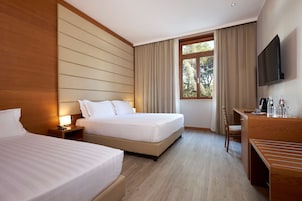 A hotel room with two beds, a desk, a chair, a TV, and a window with curtains.