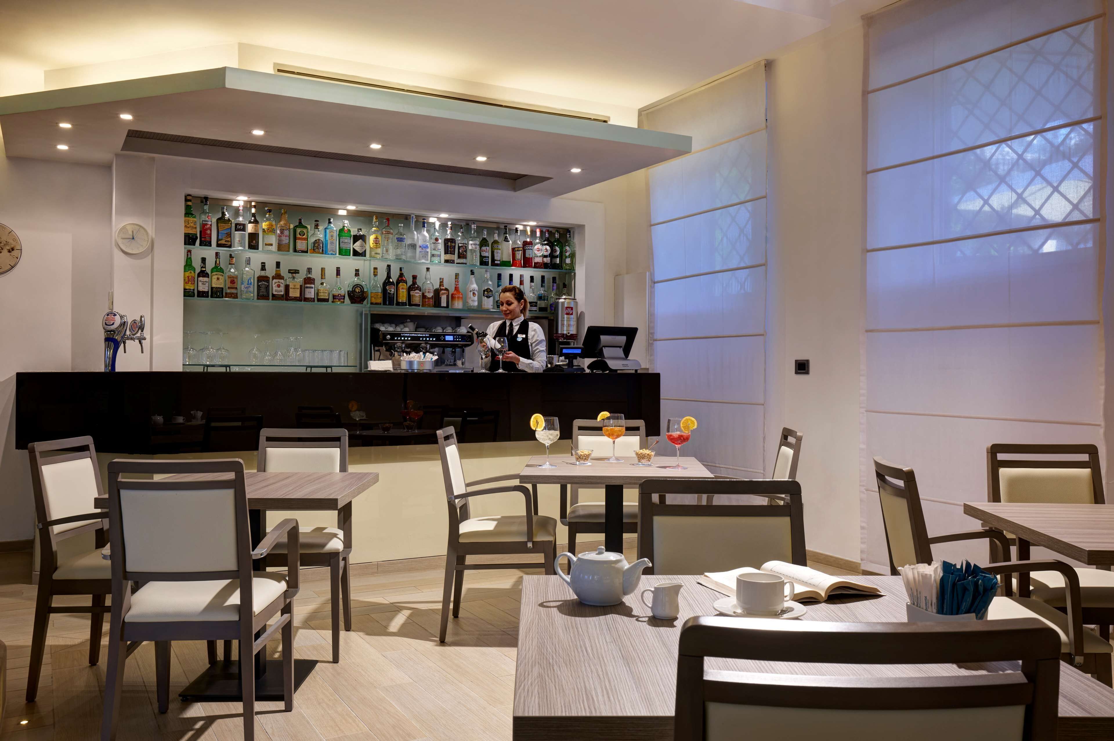 Un restaurante con zona de bar, mesas y sillas, y un reloj en la pared.