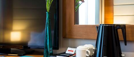 En hotelreception med en velkomstskilt, kaffemaskine, blomster i en vase og et fjernsyn i baggrunden.