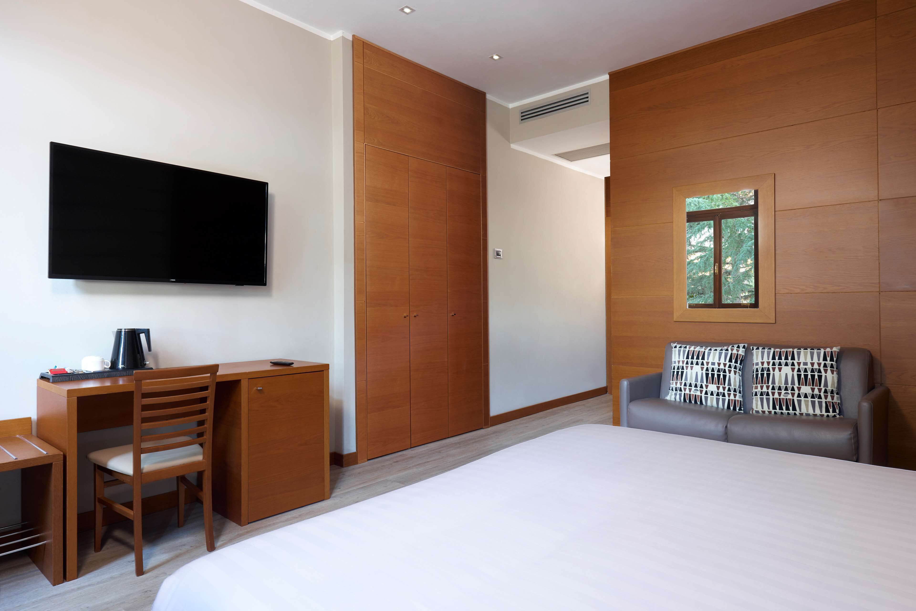 A hotel room with a bed, a desk with a chair, a television, and a wardrobe.