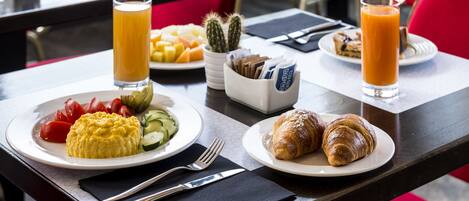 A breakfast table with plates of food, including croissants, a fruit salad, and a glass of orange juice.