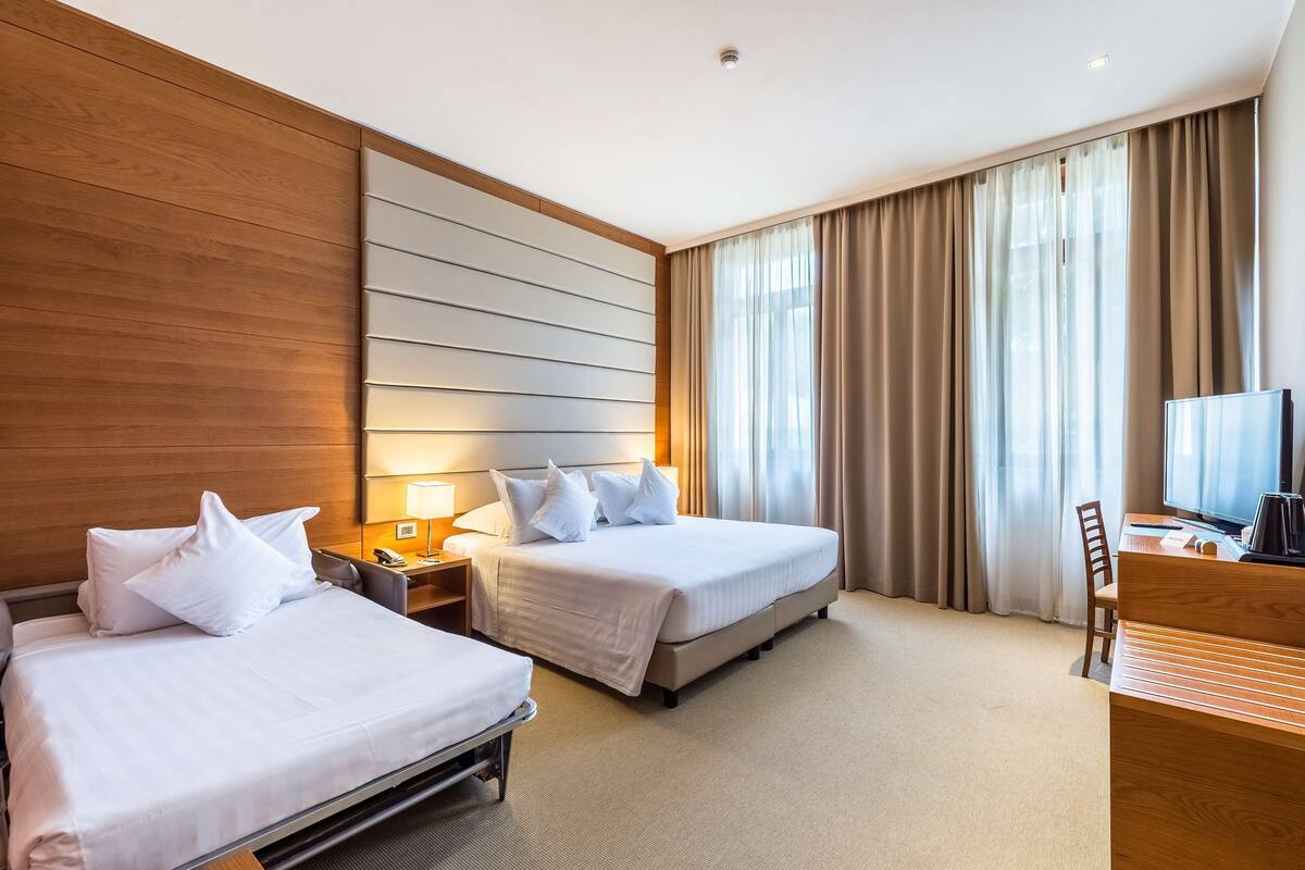 Habitación de hotel con dos camas, un escritorio, una silla, un televisor y una ventana con cortinas.