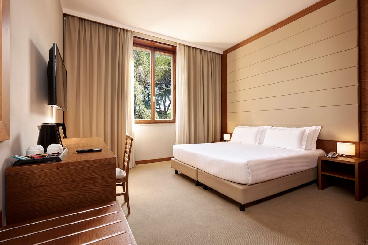 Una habitación de hotel con cama, mesita de noche, televisión y escritorio con silla.