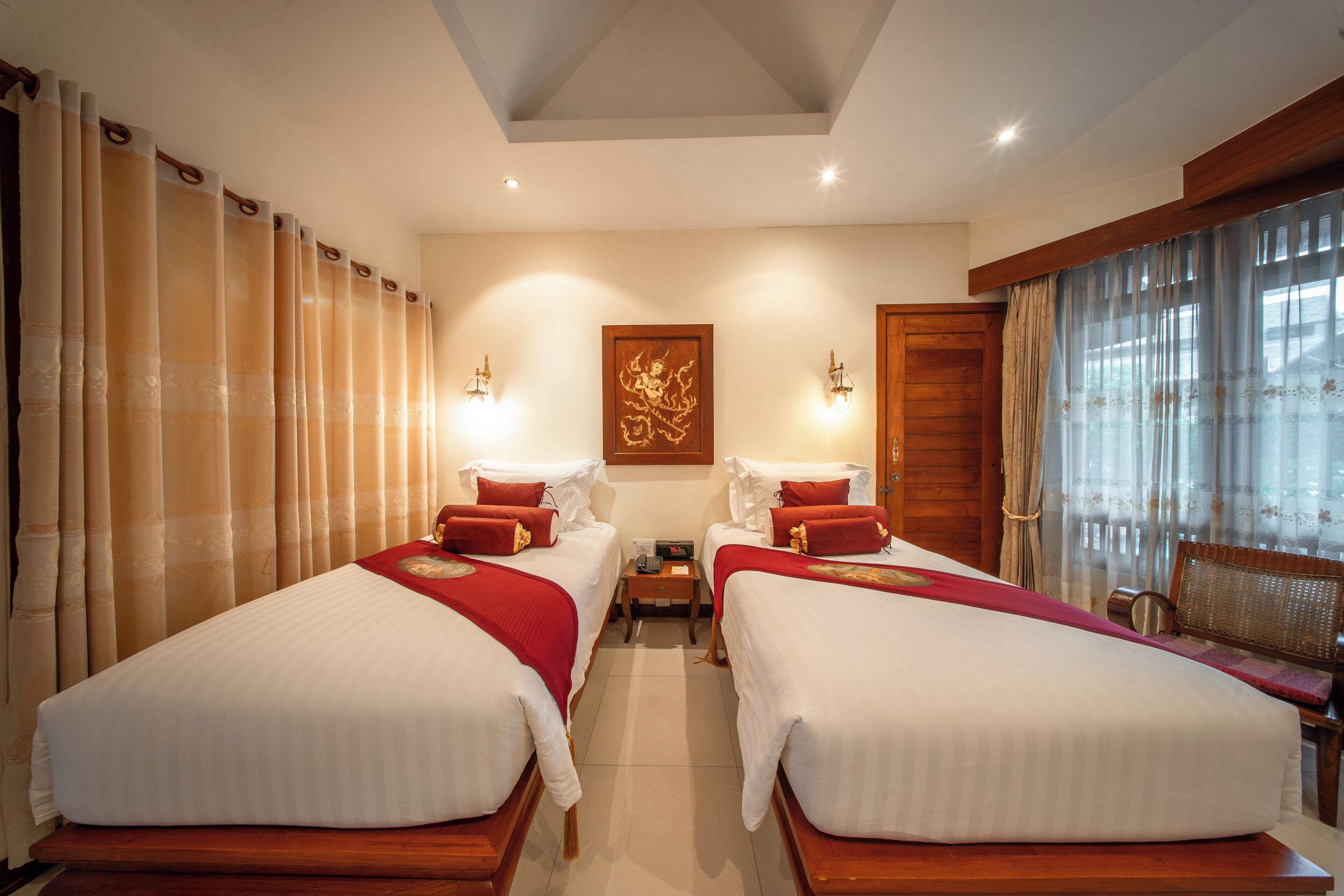 A hotel room with two beds, a wooden bench, a nightstand, and a window with curtains.
