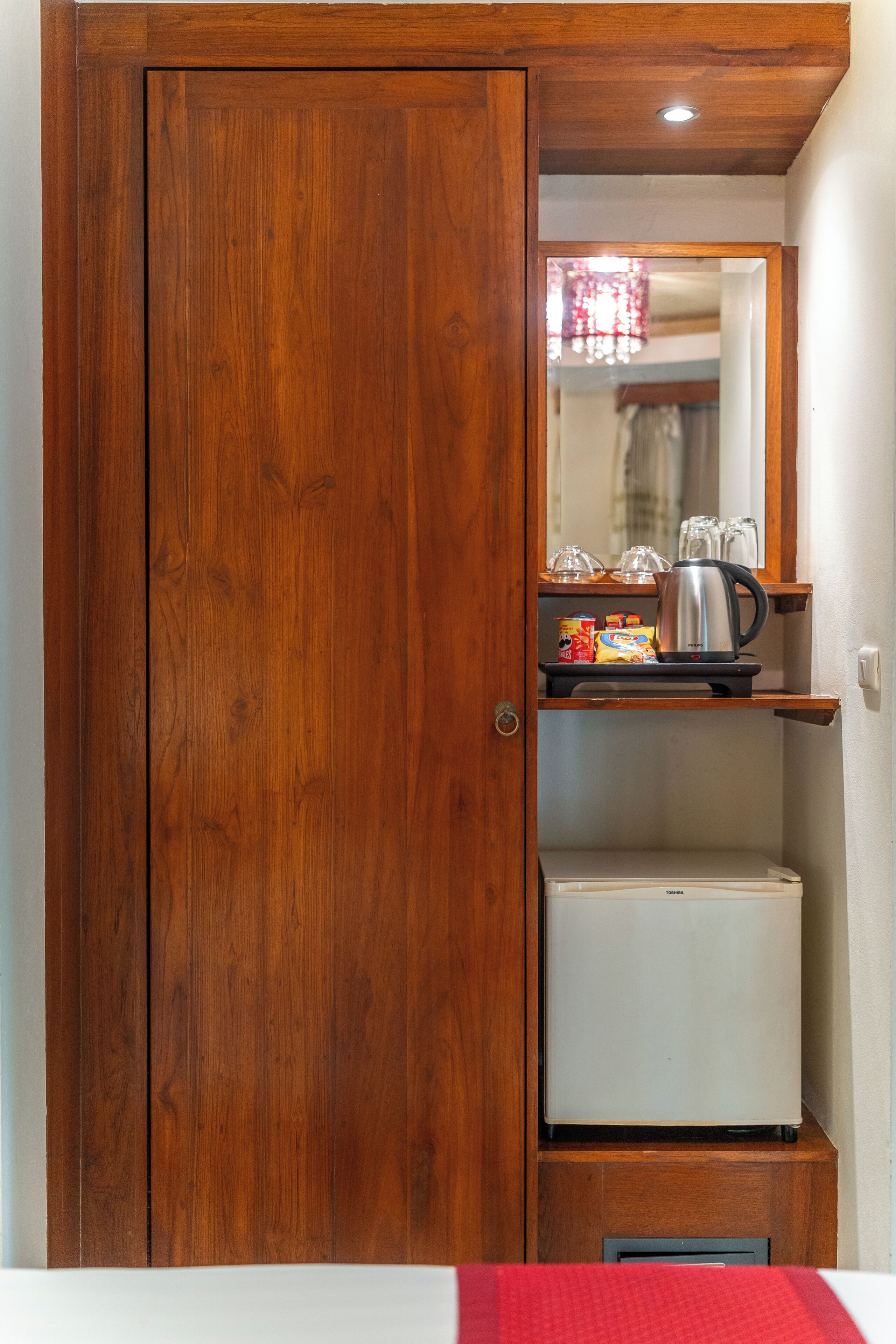Un armario de madera con un espejo, una estantería con gafas, una tetera y un refrigerador pequeño.