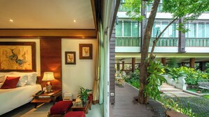 Une chambre d’hôtel avec un lit, une table de chevet, une lampe, une chaise et une table. Elle dispose d’un balcon avec vue sur un jardin et un immeuble.
