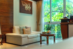 A room with a white sofa, a wooden coffee table, a framed artwork on the wall, and a view of greenery through a window. - Kodchasri Thani Hotel Chiangmai (Chiang Mai)