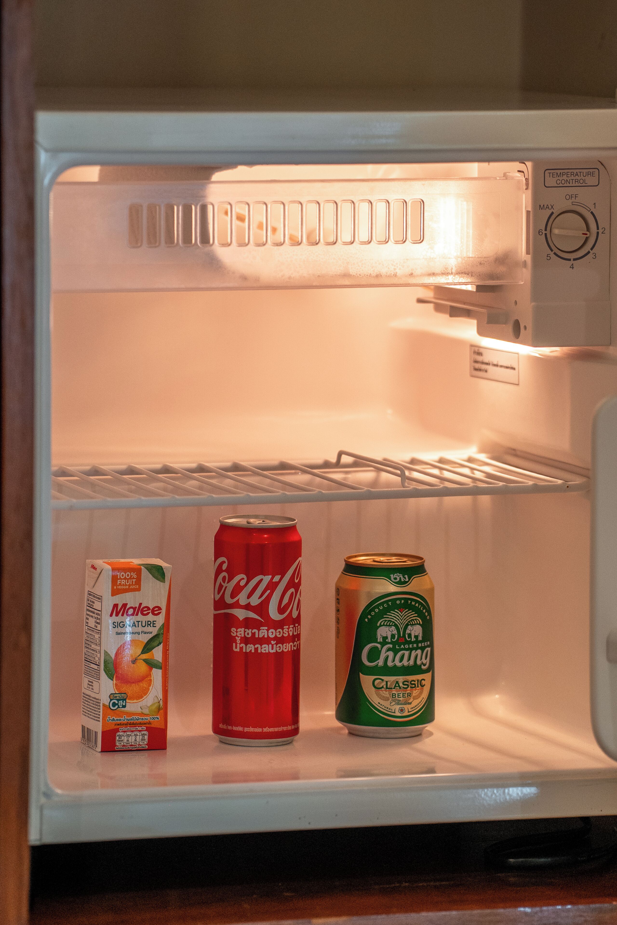 Un refrigerador abierto con un cartón de leche, una lata de Coca-Cola y una lata de cerveza Chang.