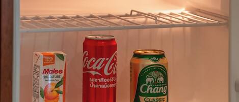 Un refrigerador abierto con un cartón de leche, una lata de Coca-Cola y una lata de cerveza Chang.