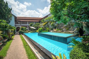 A swimming pool with a stone pathway, lush greenery, and a building with a tiled roof in the background. - Kodchasri Thani Hotel Chiangmai (Chiang Mai)