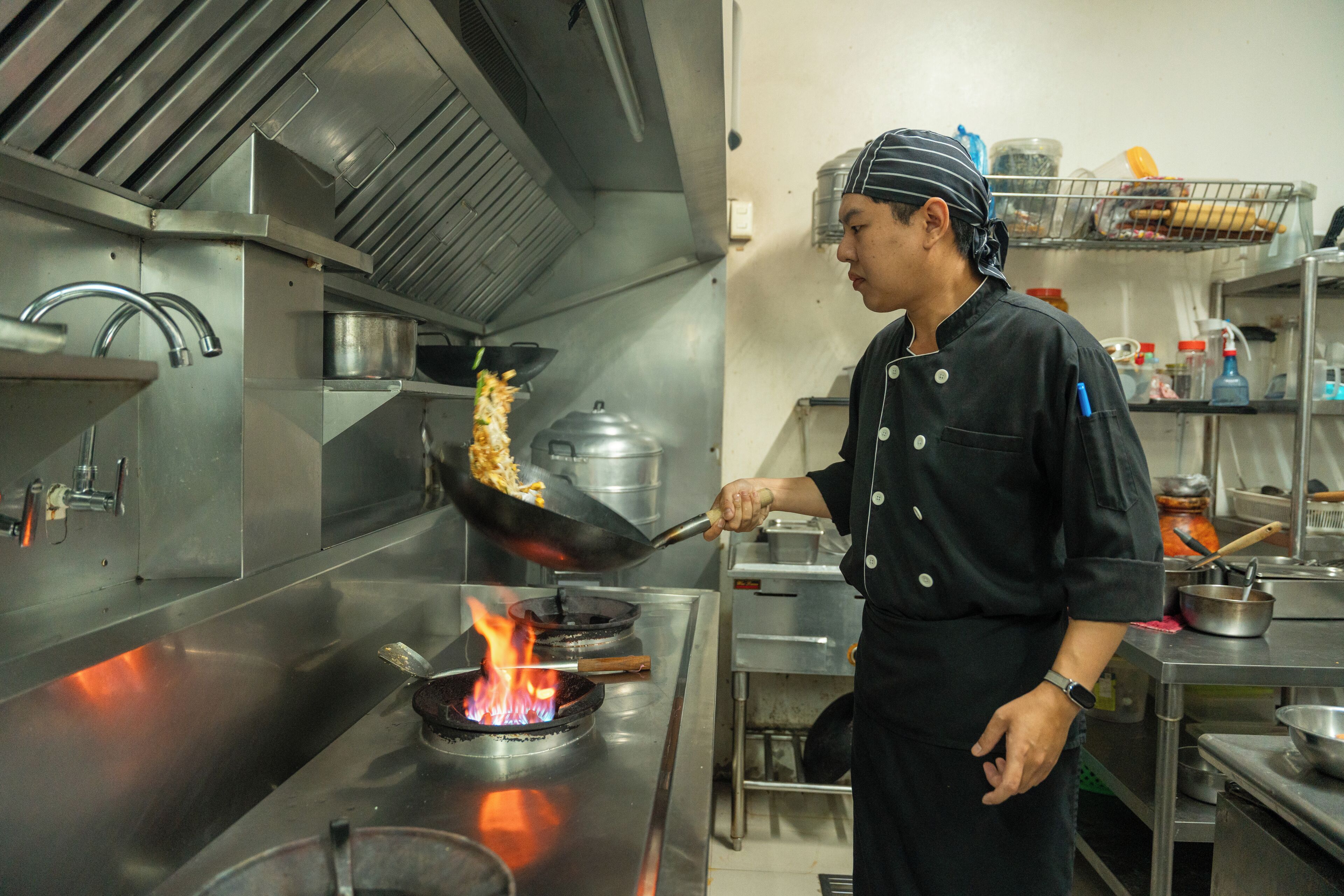 A chef cooking with a pan on a stove in a commercial kitchen.