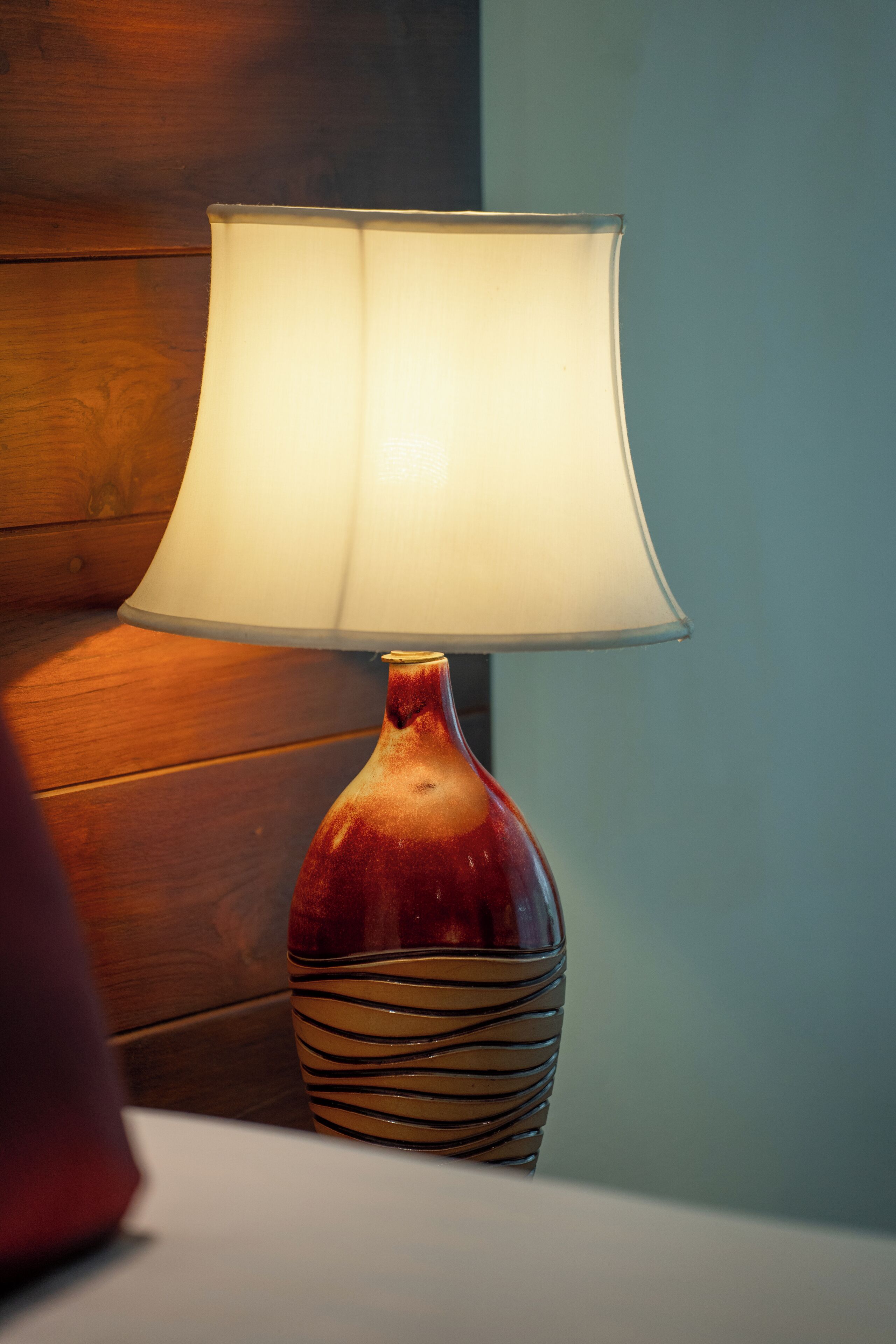 En lampa med en vit lampskärm placerad på en träyta.