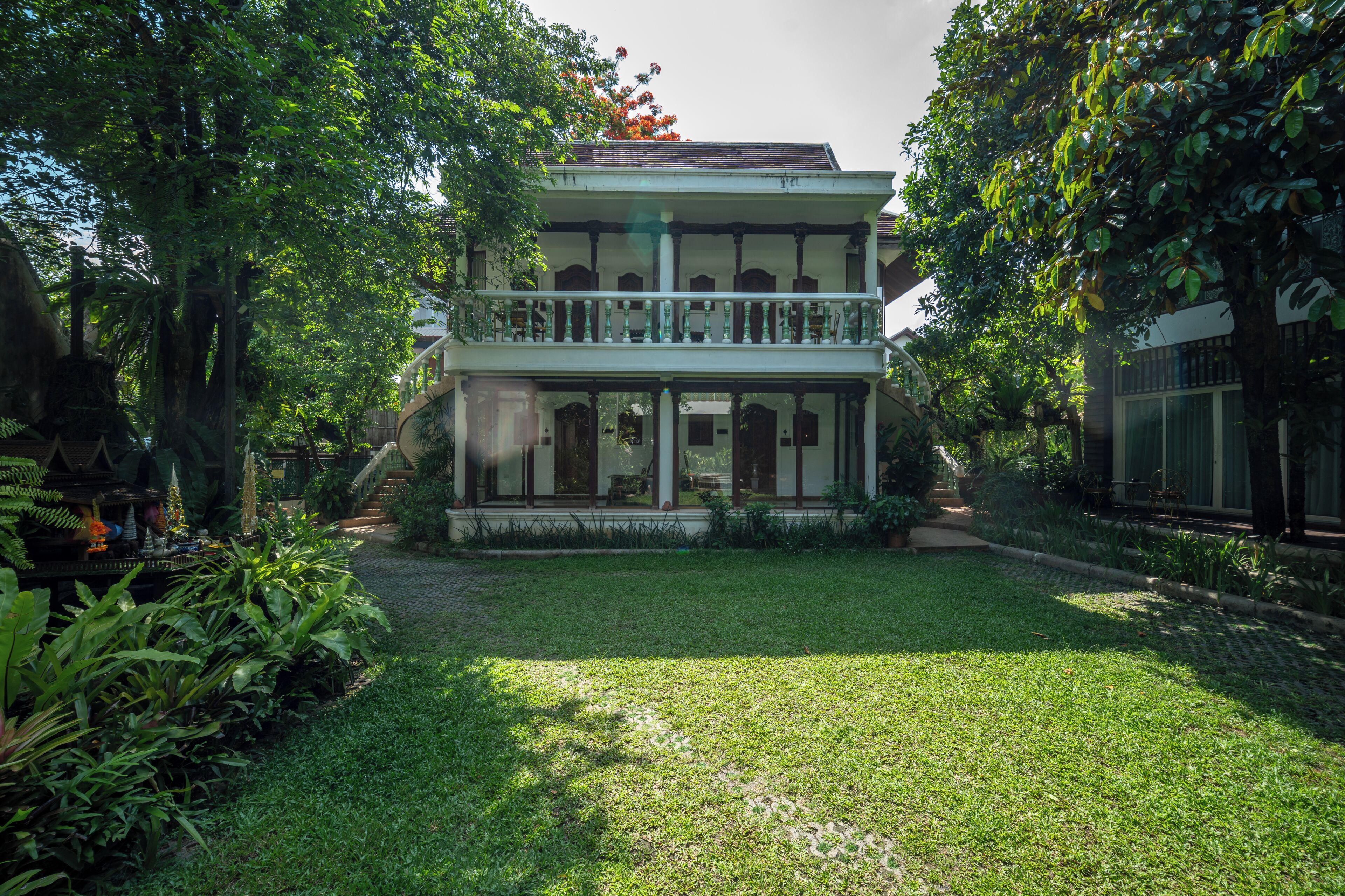 A two-story house with a balcony, surrounded by lush greenery.