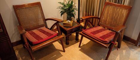 Two wooden chairs with woven backs and red cushions, a small table with a plant, and a curtain in the background.