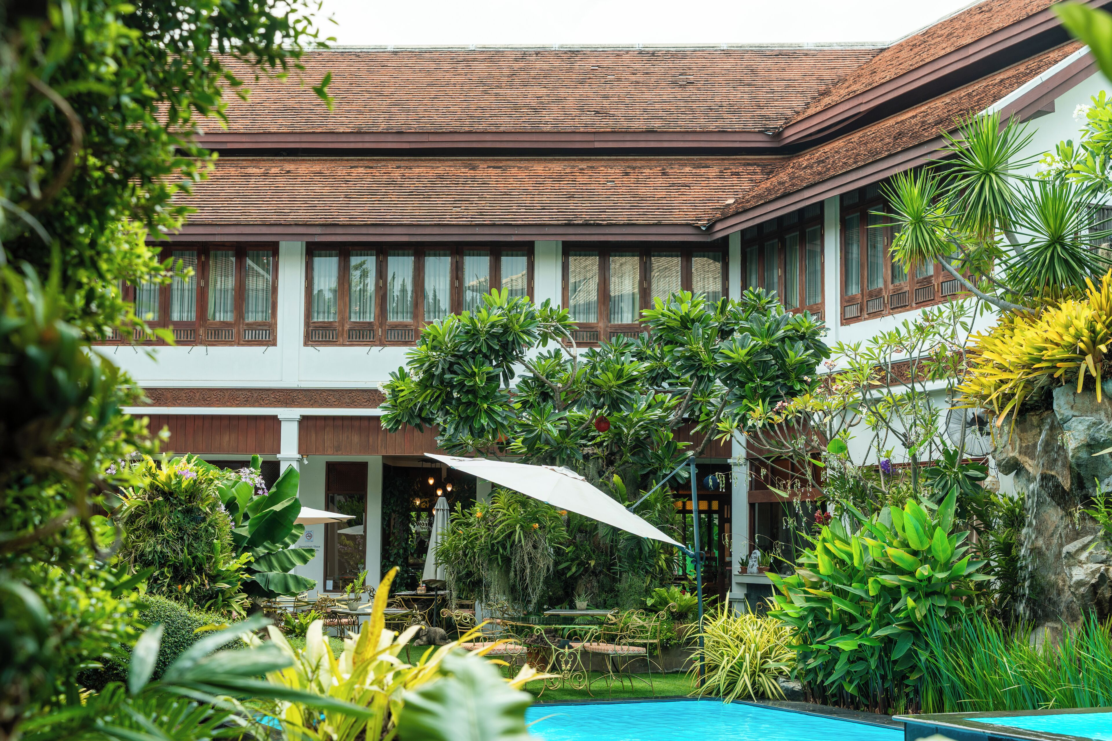 A traditional building with a tiled roof, surrounded by lush greenery and a swimming pool.