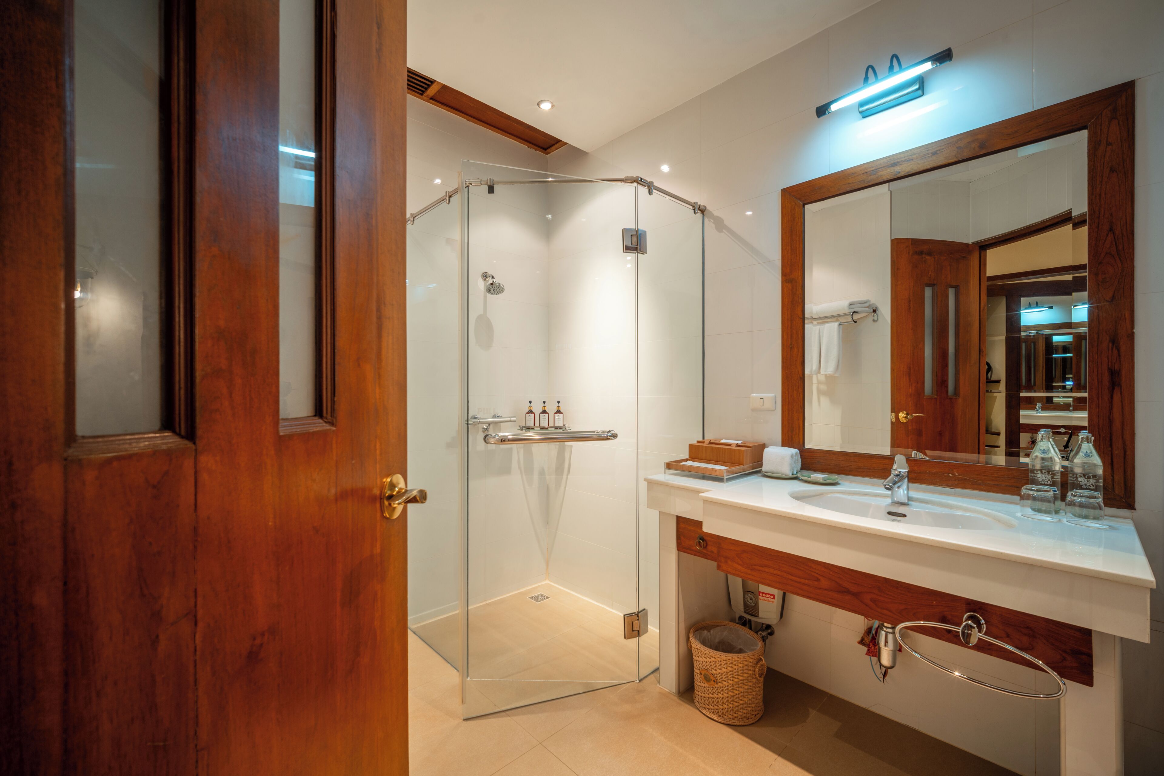 Un baño moderno con cabina de ducha de vidrio, tocador de madera con lavabo y un espejo grande.