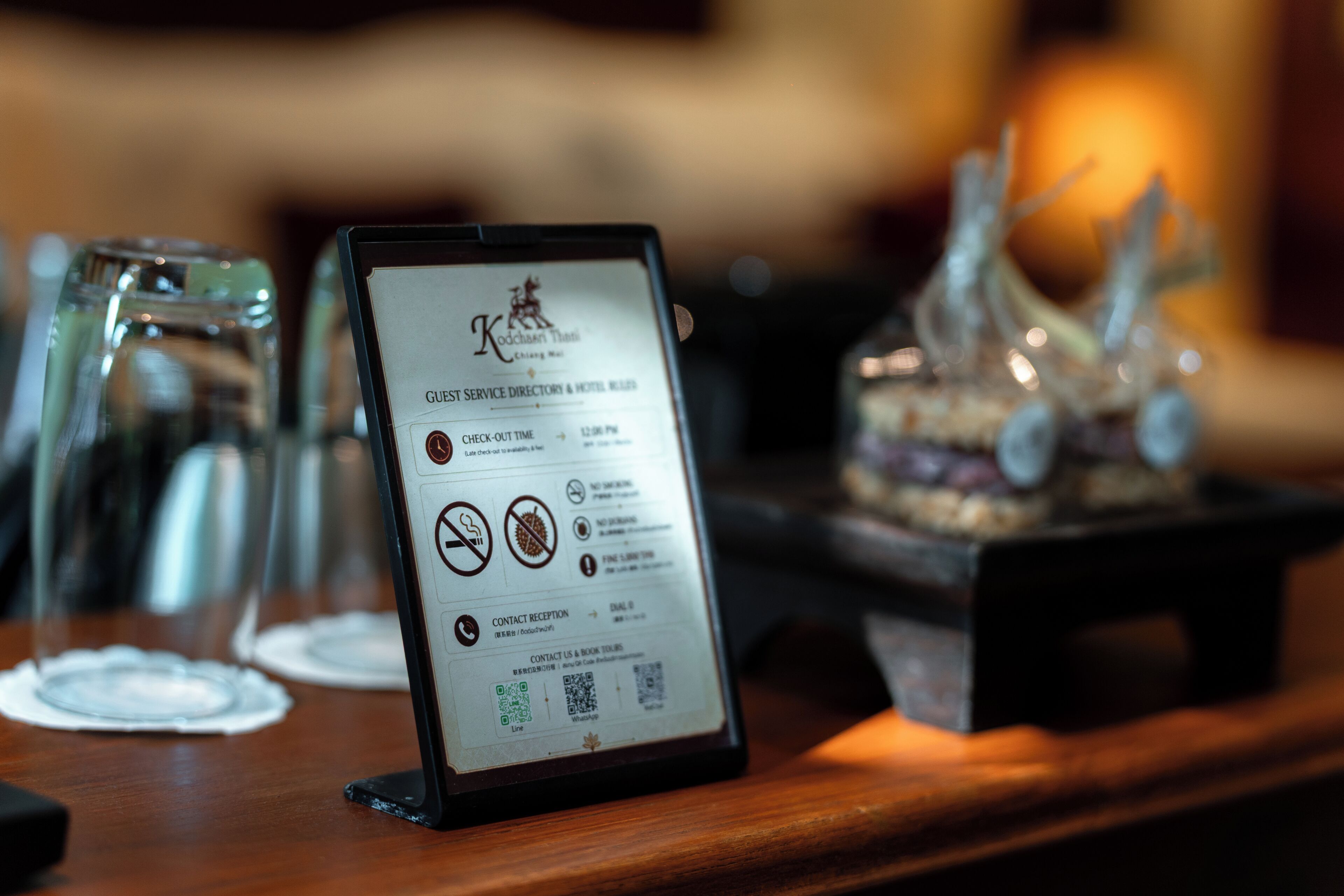 A tablet displaying a guest service directory and hotel information, placed on a wooden table with glasses and a decorative item in the background.