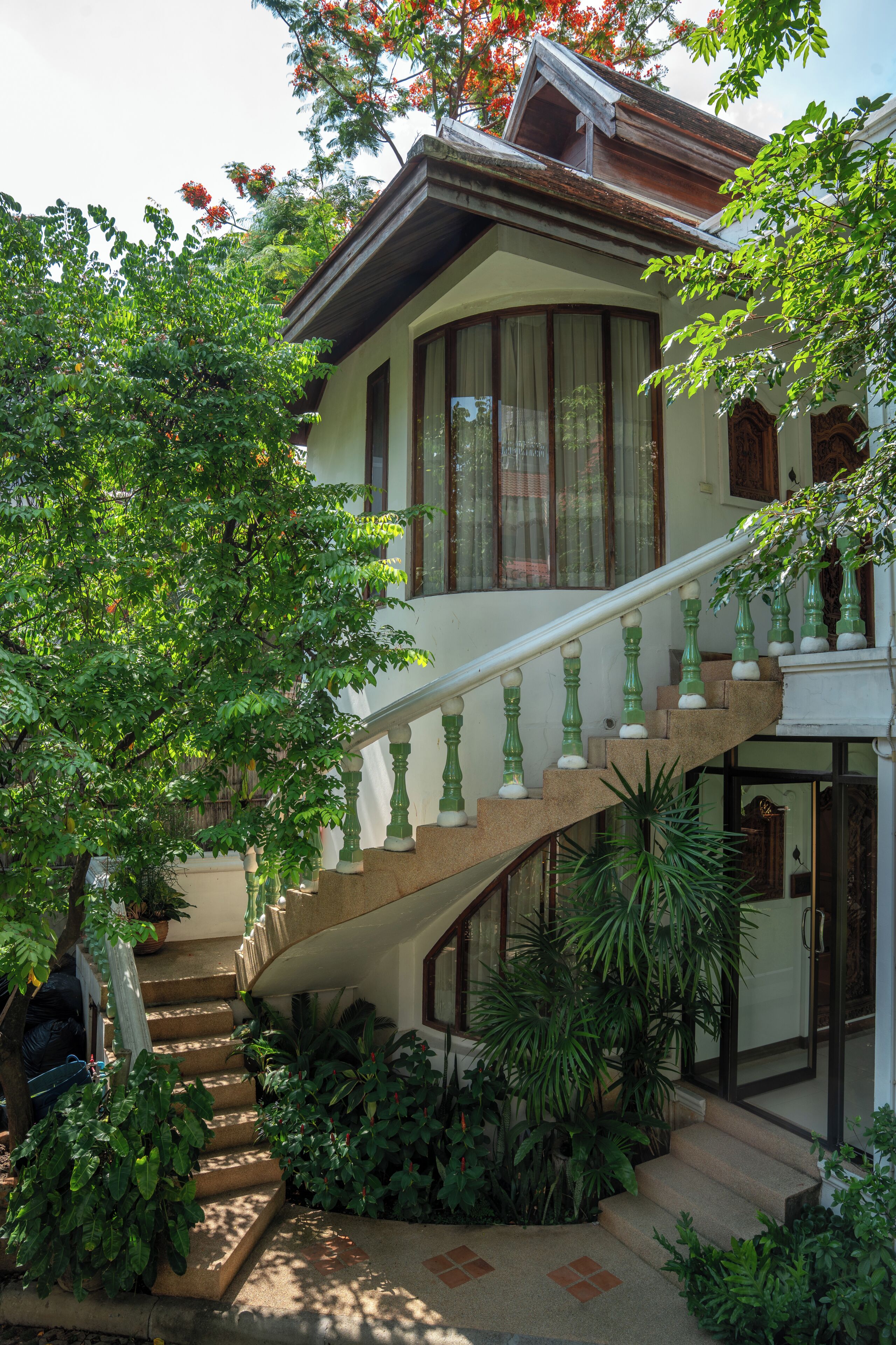 A house with a curved staircase, a large window, and lush greenery.
