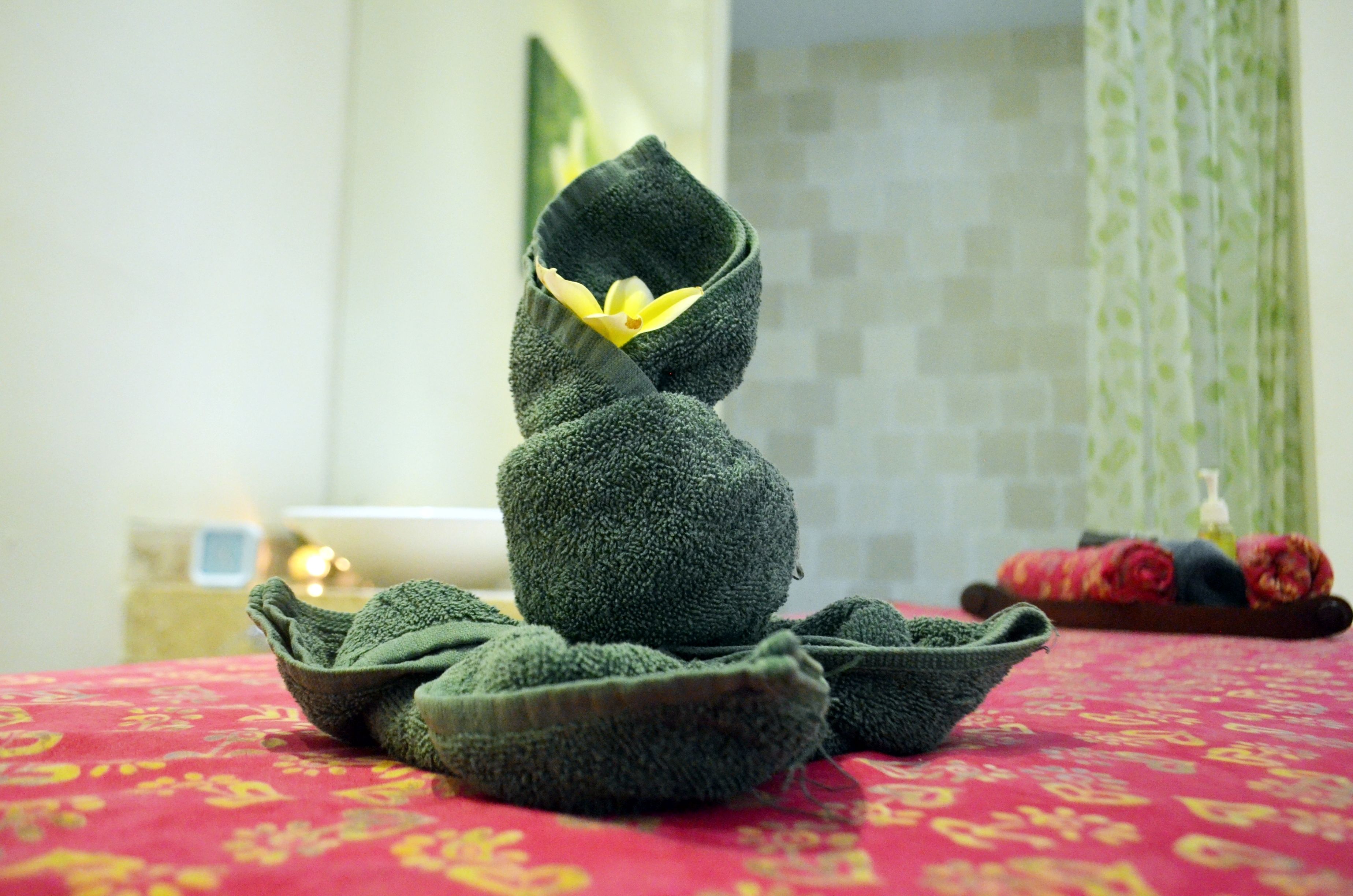 A neatly arranged towel stack on a patterned bedspread, with a candle and a bottle in the background.
