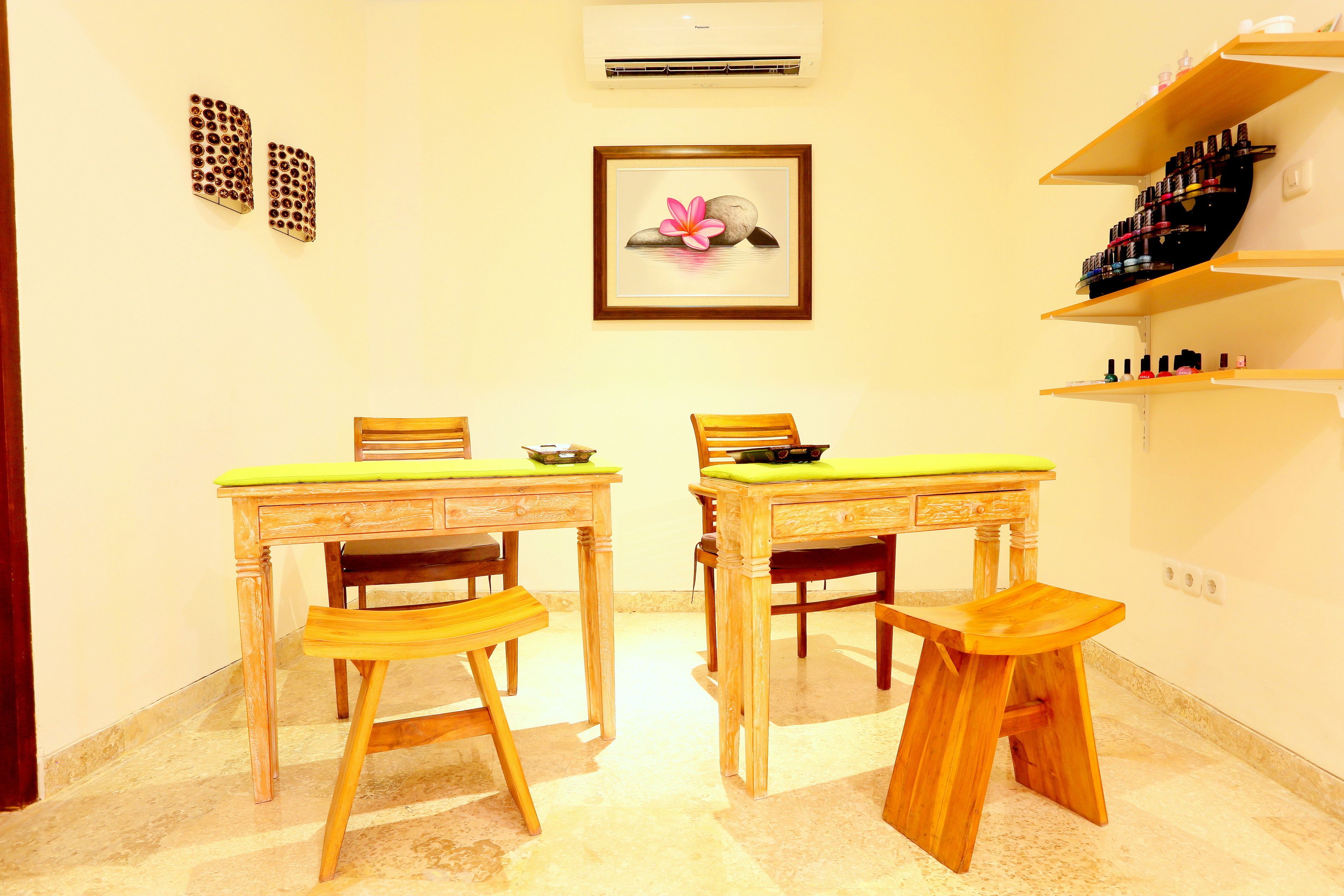 A room with two wooden tables, each with a green cushion, and a wooden stool. There are two chairs, one at each table. A framed picture of a flower is on the wall.
